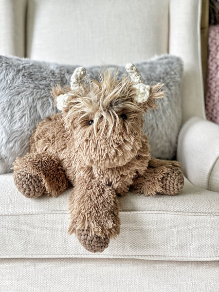 A plush highland cow stuffed animal with soft brown faux fur and crocheted accents.