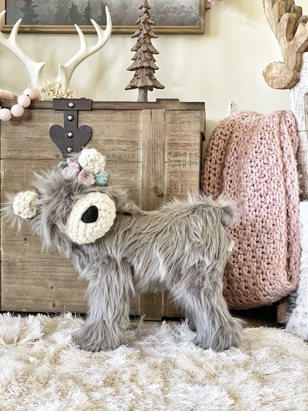 A plush standing bear with gray faux fur and crochet accents. The bear is displayed in a woodland themed nursery with a pink blanket in the background.