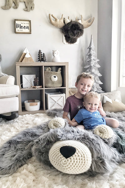 Two children sitting on a large gray bear rug made by ClaraLoo in a woodland themed bedroom.