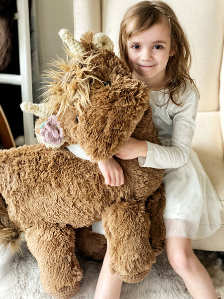 A child holding a large highland cow plush animal made by ClaraLoo with soft brown faux fur and crochet accents.