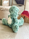A green plush T-Rex stuffed animal made by ClaraLoo with crocheted accents in a dinosaur themed nursery.