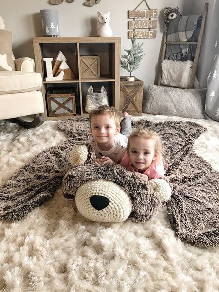 A large brown bear rug on the floor of a woodland themed kids bedroom. The bear rug is made by ClaraLoo with plush faux fur and crocheted accents.