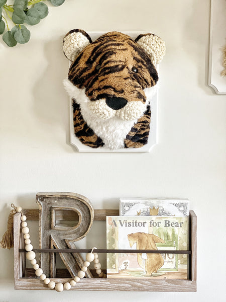 A plush Tiger Wall Mount handmade by ClaraLoo with striped orange and black faux fur and crocheted accents. This stuffed tiger is mounted on a white wooden plaque that is hung on the wall of a safari themed nursery.