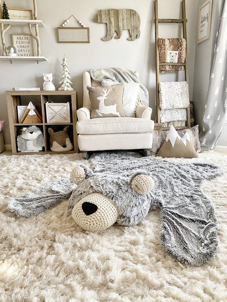 A woodland themed nursery with a plush bear rug made by ClaraLoo on the floor. The bear rug has plush gray faux fur with a cream colored face and ears.
