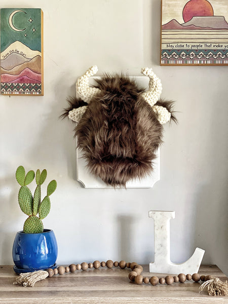 A plush Bison Wall Mount handmade by ClaraLoo in a western themed cowboy nursery. The stuffed bison is made of soft brown faux fur with cream colored crocheted ears and horns.  The bison is mounted on a white wooden plaque.