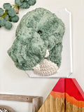 A plush T-Rex Wall Mount handmade by ClaraLoo in a dinosaur themed nursery. This stuffed dinosaur is made with soft green faux fur and crocheted accents. This plush T-Rex is mounted on a white wooden plaque.
