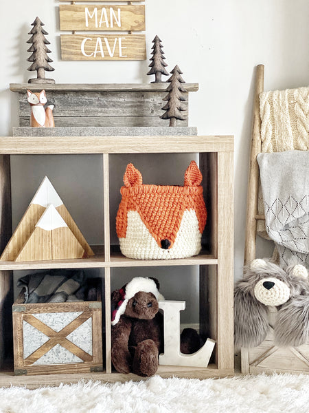 Handmade crocheted Fox Basket sitting on a wooden shelf. The fox basket is orange and white with a black nose.